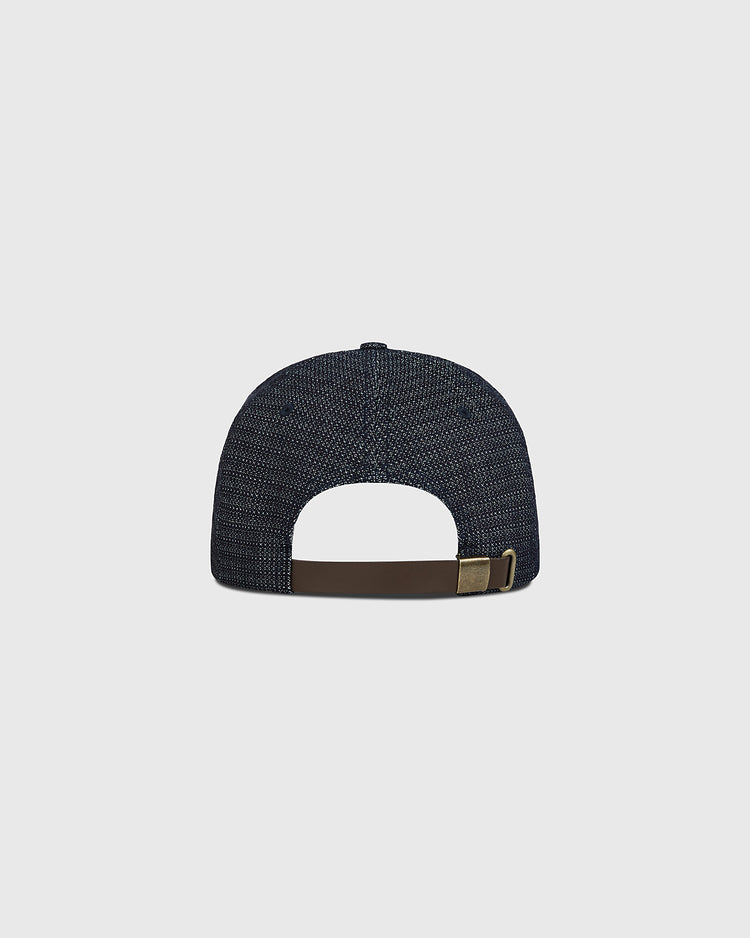 The Ebbets Field Hiroshima Carp Japanese Indigo Cotton Dobby Ballcap is displayed from the back, showcasing its dark blue indigo-dyed textured finish, premium Japanese cotton construction, and a brown adjustable strap with metal clasp, all set against a plain light gray background.