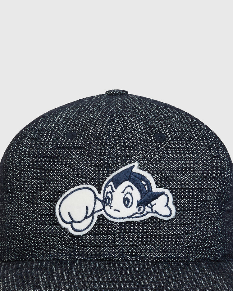 A close-up of the Ebbets Field Sankei Atoms Japanese Indigo Cotton Dobby Ballcap, showcasing an embroidered spiky-haired cartoon character with a raised fist on the front, celebrating the legacy of Sankei Atoms and Japanese baseball history.