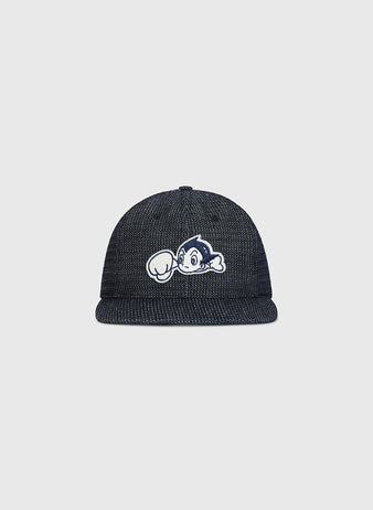 The Ebbets Field Sankei Atoms Japanese Indigo Cotton Dobby Ballcap, inspired by Japanese baseball history, features a cartoon character with a raised fist embroidered on the front. The indigo-dyed cap’s textured cotton stands out against a plain light gray background.