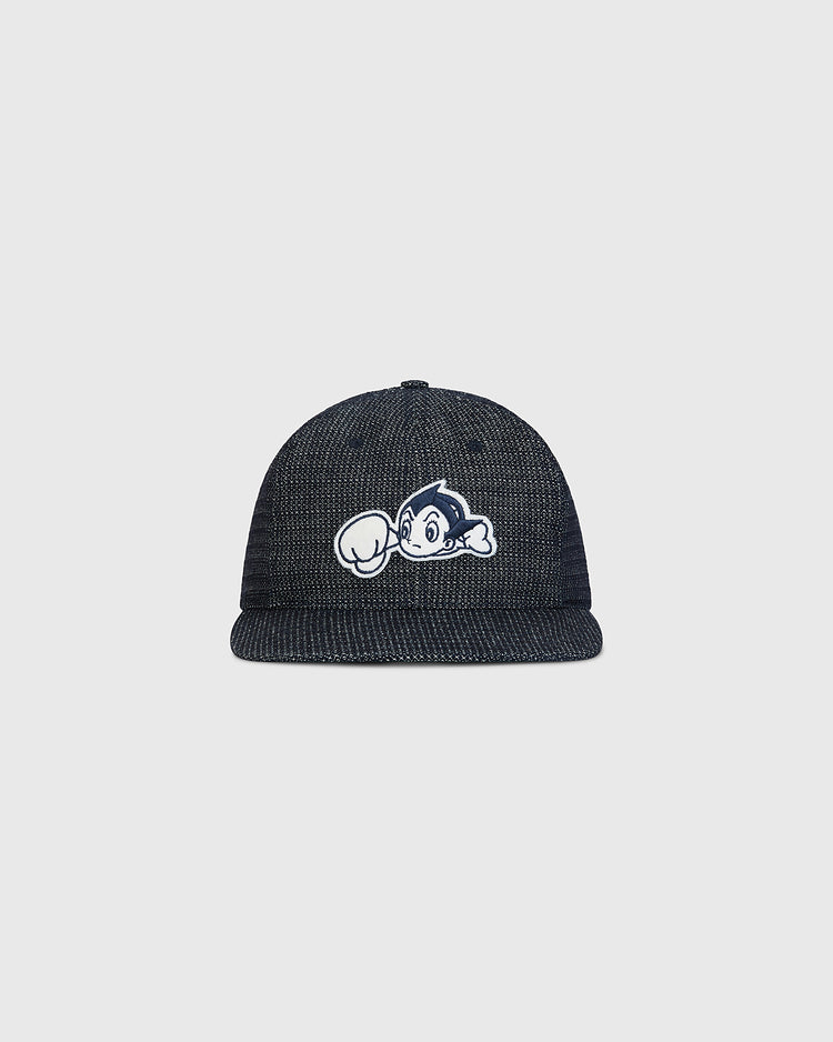The Ebbets Field Sankei Atoms Japanese Indigo Cotton Dobby Ballcap, inspired by Japanese baseball history, features a cartoon character with a raised fist embroidered on the front. The indigo-dyed cap’s textured cotton stands out against a plain light gray background.