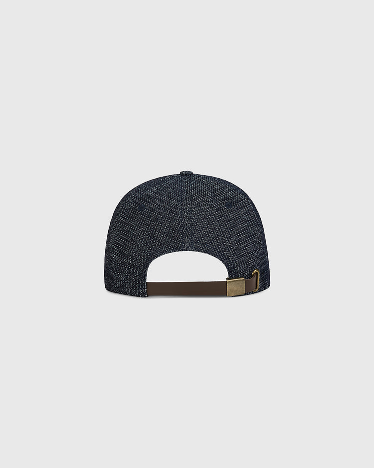 The Ebbets Field Tokyo Giants 1940 Japanese Indigo Cotton Ballcap is displayed from the back, highlighting its textured dark blue fabric and an adjustable brown strap with a metal clasp. The cap is set against a plain, light gray background.