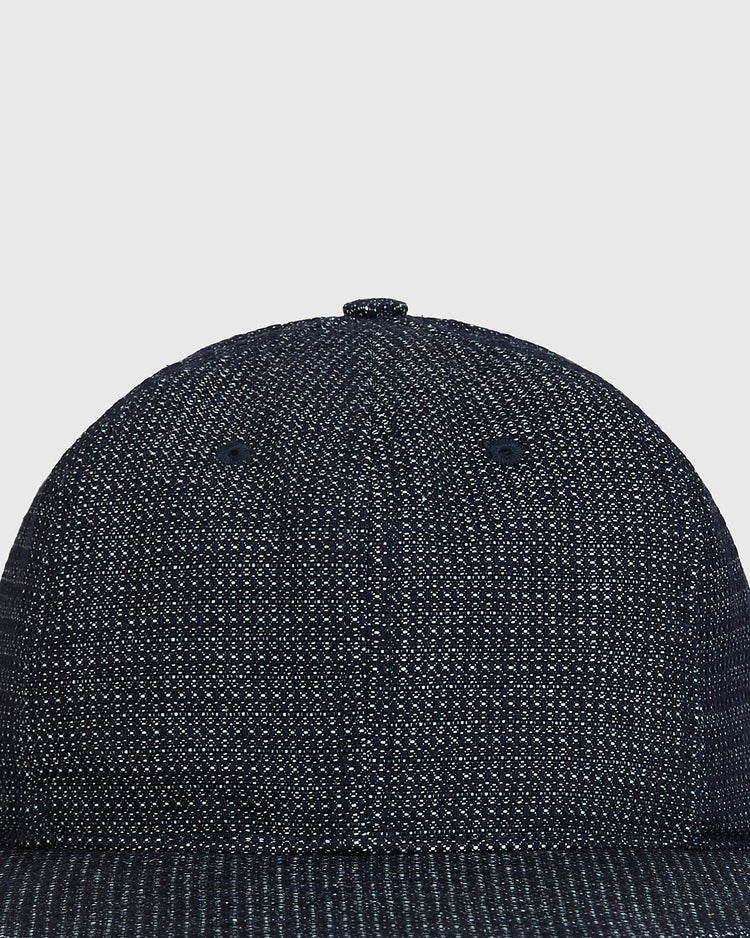 A close-up of the top front of the Ebbets Field Blank Japanese Indigo Cotton Dobby Ballcap, crafted from indigo-dyed Japanese cotton with a textured speckled pattern and finished with a small button on top.