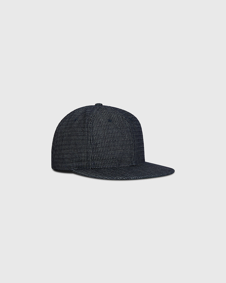 A Blank Japanese Indigo Cotton Dobby Ballcap by Ebbets Field, featuring a dark textured finish and flat brim, displayed against a plain light gray background.