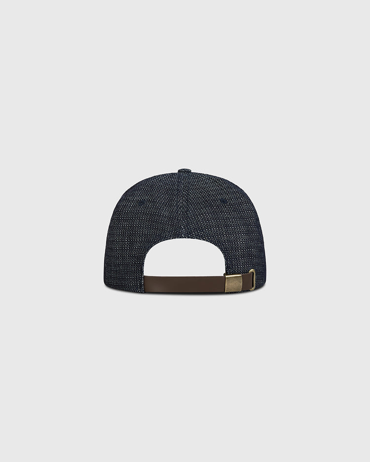 Shown on a plain light gray background, the Ebbets Field Blank Japanese Indigo Cotton Dobby Ballcap is pictured from the back, displaying its indigo-dyed, dark blue textured cotton finish and featuring a brown adjustable strap with a brass buckle.