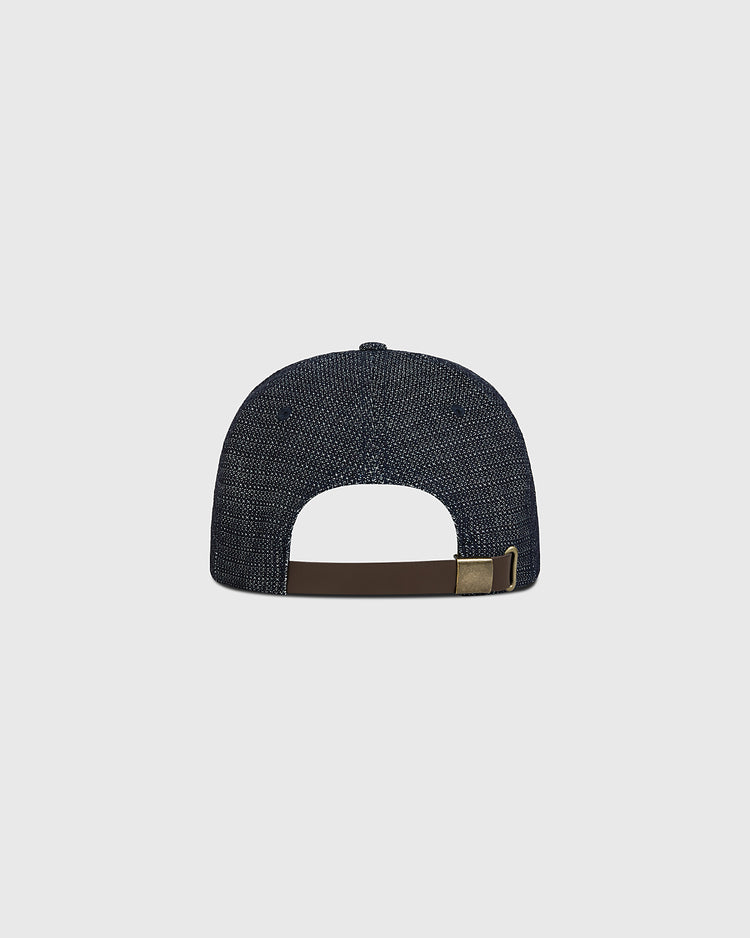 The Ebbets Field Fuji Athletic Club Japanese Indigo Cotton Dobby Ballcap is displayed from the back, highlighting its dark indigo dye inspired by Japanese American baseball heritage. A brown adjustable strap with a brass buckle is visible, set against a plain light gray background.