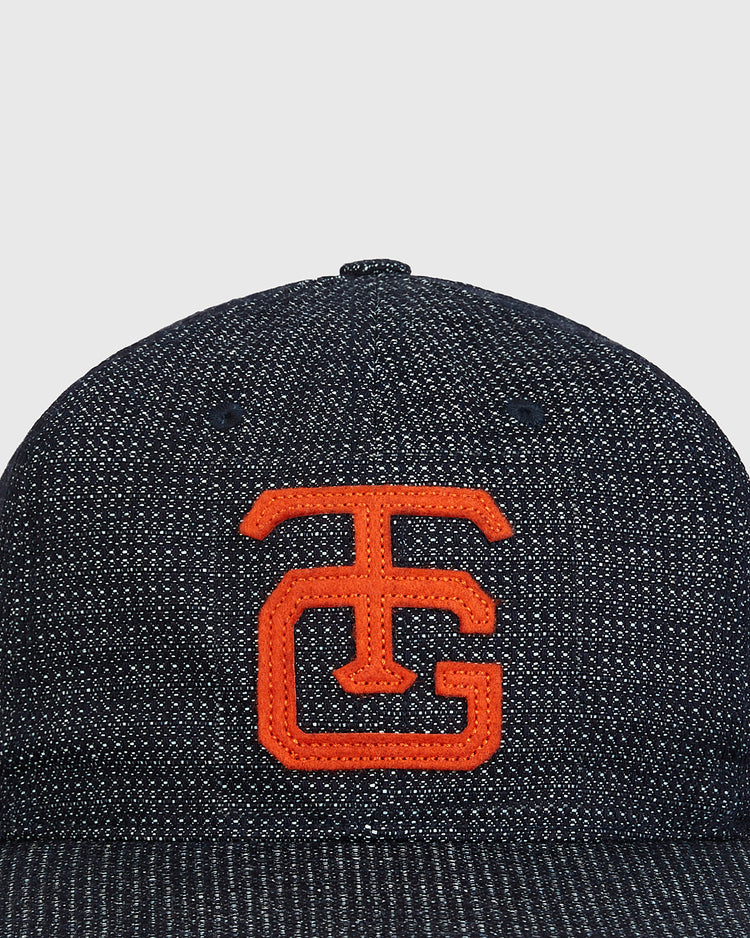 A close-up of the Ebbets Field Tokyo Giants 1953 Japanese Indigo Cotton Dobby Ballcap, showcasing its dark textured fabric and orange embroidered “TG” letters on the front.
