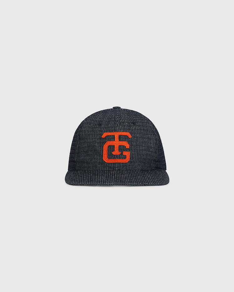 An Ebbets Field Tokyo Giants 1953 Japanese Indigo Cotton Dobby Ballcap, featuring a textured dark blue design and a bold red embroidered TG logo on the front, is displayed against a plain light gray background.
