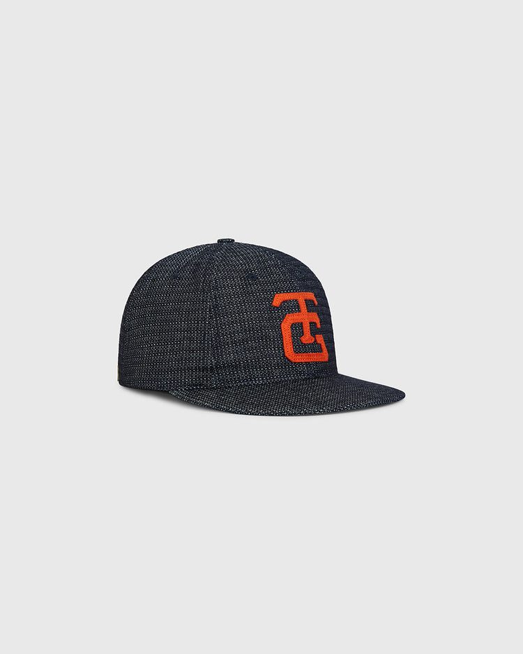 Tokyo Giants 1953 Japanese Indigo Cotton Dobby Ballcap by Ebbets Field shown against a plain light gray background, featuring a dark gray textured fabric with a flat brim and an orange interlocking letter design on the front.