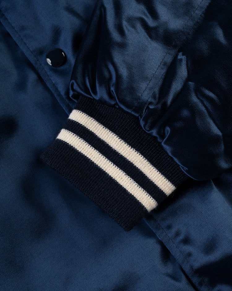 Close-up of an EFF Philadelphia Athletics 1953 Authentic All Satin Varsity Jacket sleeve in navy blue with a ribbed cuff featuring two white stripes, black snap button, and a shiny finish inspired by classic Philly Athletics style.