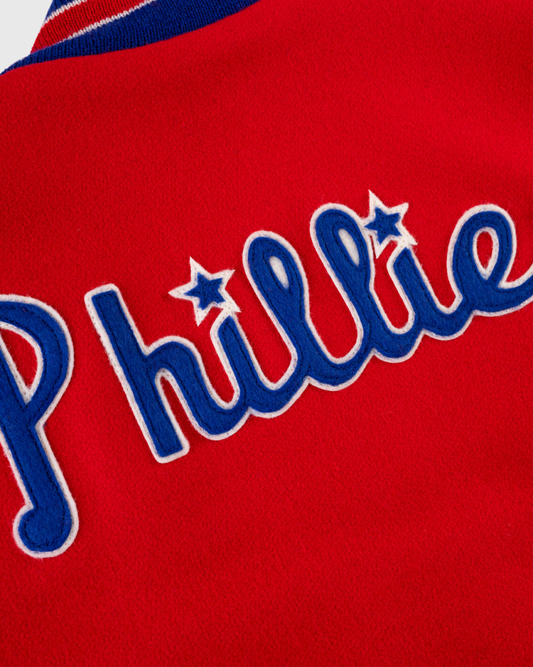 The EFF Philadelphia Phillies 1949 Authentic All Wool Varsity Jacket features red fabric with Phillies in blue and white script and stars above the “i”s, offering a classic nod to vintage baseball jacket style.