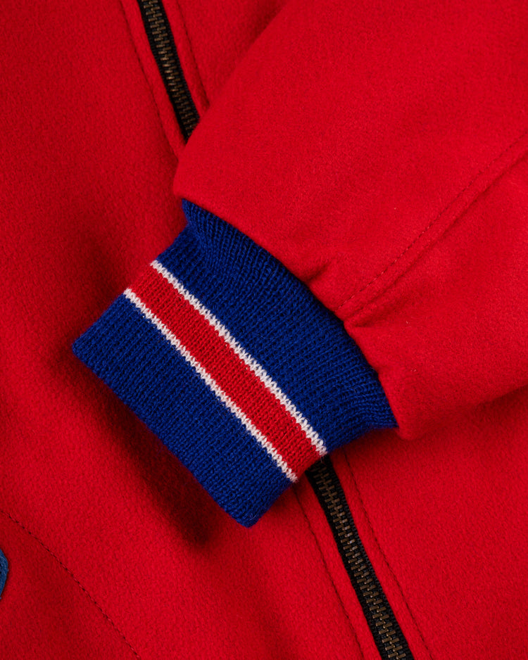 Close-up of an EFF Philadelphia Phillies 1949 Authentic All Wool Varsity Jacket sleeve in red with a blue, white, and red striped knit cuff next to a black zipper. The thick fabric looks warm.