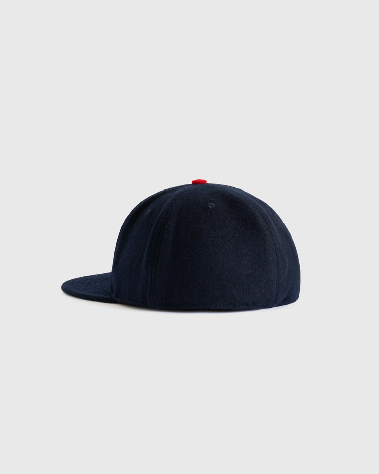 The EFF Minneapolis Millers 1938 Authentic Wool Ballcap is shown from the side. This navy blue cap features a red top button and is set against a plain light gray background.