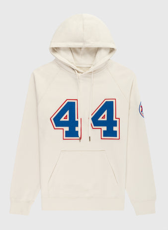 The EFF Hank Aaron French Terry Script Hooded Sweatshirt features a cream color, large blue and red number 44 honoring Hank Aaron of the Milwaukee Braves, a circular patch on the left sleeve, front pocket, and drawstring hood.