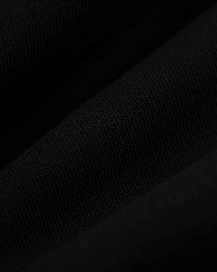 Close-up of black fabric with fine knit texture and diagonal folds, reflecting the vintage style of the EFF Roberto Clemente French Terry Feld Pullover Hoodie. Subtle shadows and highlights add a sense of movement to the material.