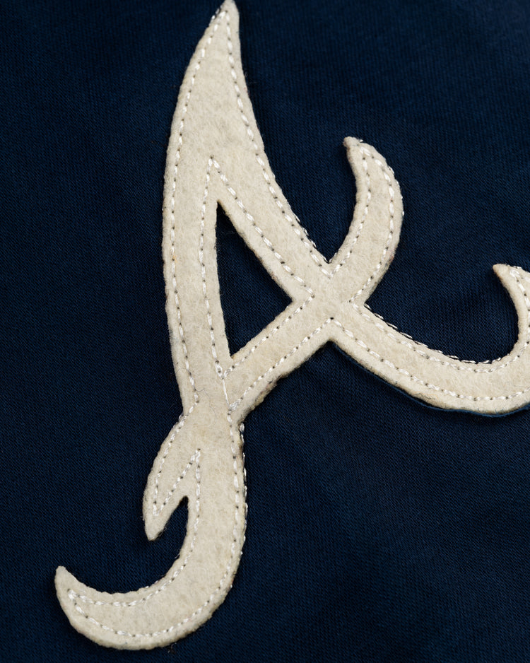A cream A is sewn onto a dark blue fabric, echoing the 1968 Braves logo featured on the EFF Atlanta Braves 1968 Satin Windbreaker Jacket.