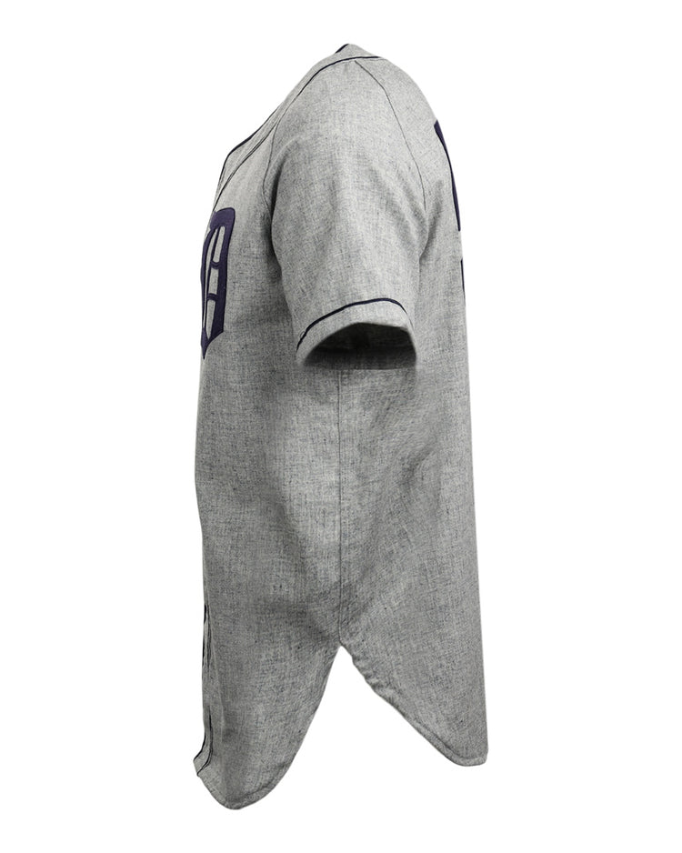 Side view of the EFF Duke University 1953 Road Jersey, a gray short-sleeve button-up with dark blue trim, partial numbers on front and back, curved hem, and textured fabric, inspired by the College Vault baseball jersey.