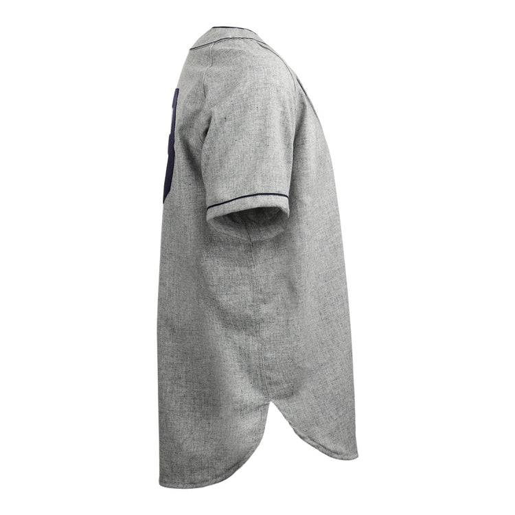 Side view of the EFF Duke University 1953 Road Jersey, a gray short-sleeve button-up shirt with dark trim on sleeve cuffs and a rounded, elongated back hem, inspired by classic College Vault style baseball jerseys.