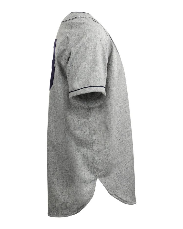 Side view of the EFF Duke University 1953 Road Jersey, a gray short-sleeve button-up shirt with dark trim on sleeve cuffs and a rounded, elongated back hem, inspired by classic College Vault style baseball jerseys.