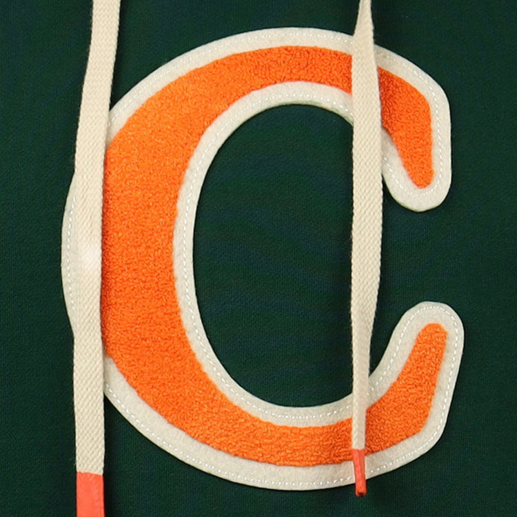 Close-up of a large orange C with a white outline on dark green fabric, partly covered by two cream drawstrings with orange tips, from the Carrots Arlington Heights Collection Hoodie by EFF.