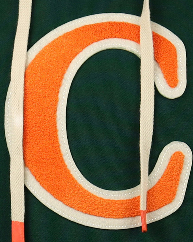 Close-up of a large orange C with a white outline on dark green fabric, partly covered by two cream drawstrings with orange tips, from the Carrots Arlington Heights Collection Hoodie by EFF.
