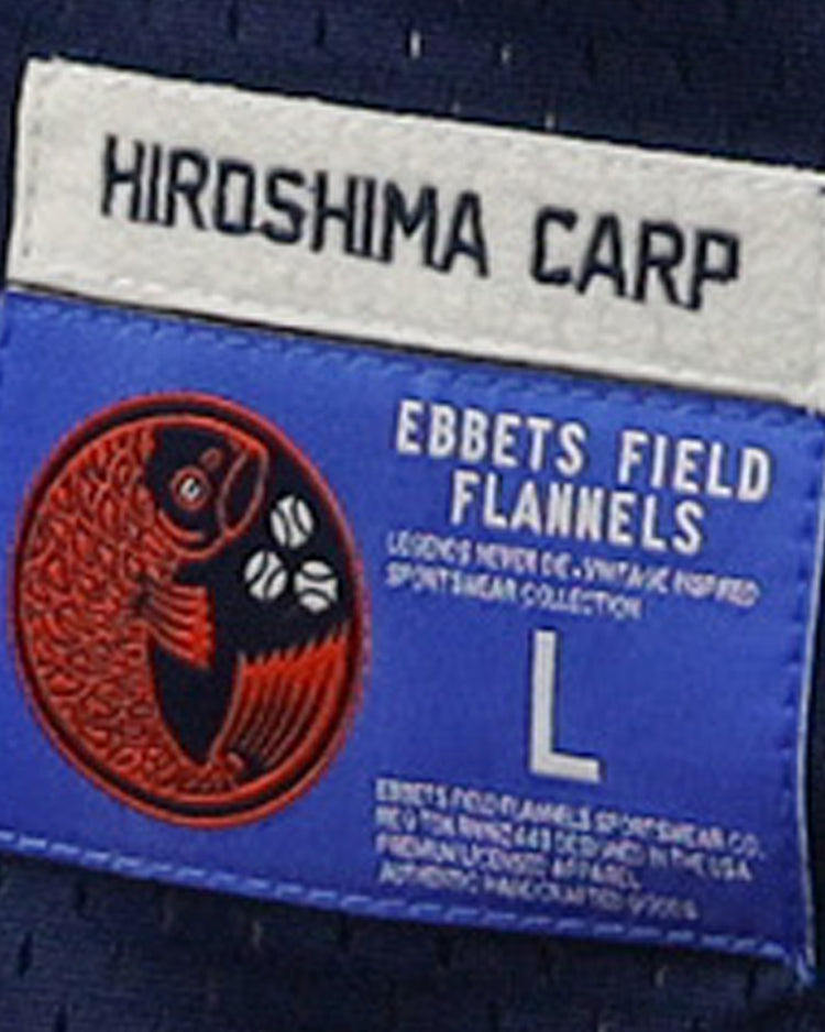 A blue and white label on the EFF Hiroshima Carp DNA Replica V-Neck Mesh Jersey features a red fish logo, size L, and vintage branding—ideal for fans of classic mesh jerseys.