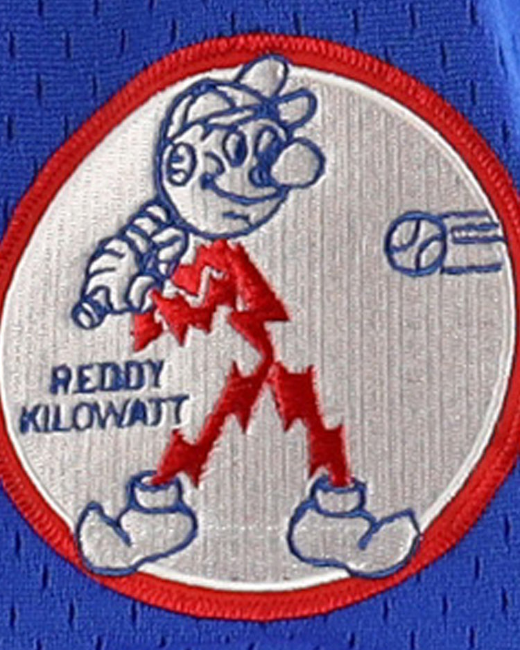 The Reddy Kilowatt EFF DNA Replica V-Neck Mesh Jersey by EFF features Reddy Kilowatt, the red lightning bolt cartoon, with a baseball bat and Reddy Kilowatt text as a ball flies in on a blue mesh-textured electric power background.