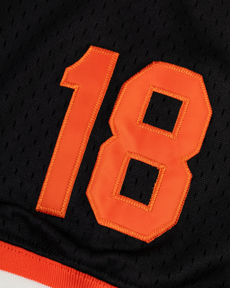 A close-up of the orange 18 with a white outline, stitched on a black EFF Tokyo Giants Mesh V-Neck Baseball Jersey, featuring vintage-inspired mesh and classic white and red stripes at the hem.