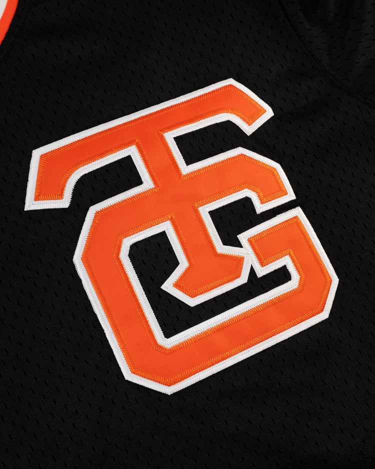A close-up of the EFF Tokyo Giants Mesh V-Neck Baseball Jersey, showcasing bold orange and white outlined TC letters intertwined on vintage-inspired black mesh fabric.