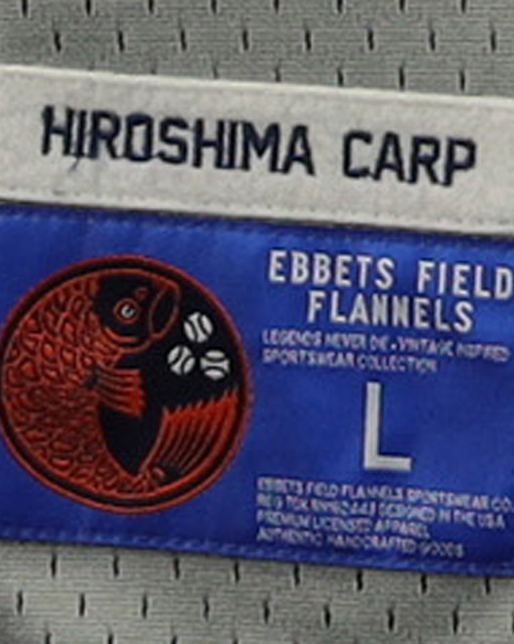 Clothing tag for the Hiroshima Carp EFF DNA Replica Button-Up Mesh Jersey by EFF, featuring “HIROSHIMA CARP” on a white label above a blue label with a red koi fish graphic, size L, and manufacturer info.