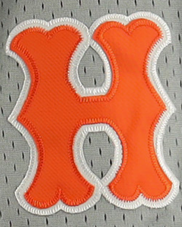 An orange, rounded letter H with a white embroidered border is sewn onto the gray mesh of the EFF Hiroshima Carp DNA Replica Button-Up Mesh Jersey, echoing vintage Japanese Central League styles.