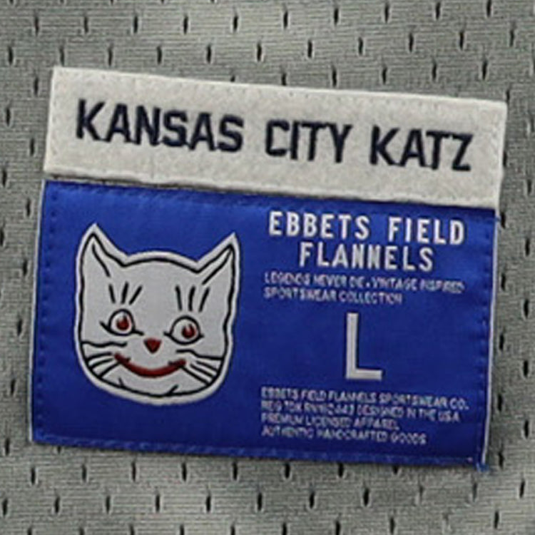 A blue and white label on the EFF Kansas City Katz DNA Replica Button-Up Mesh Jersey features a white cat face with red details, “Kansas City Katz,” “Ban Johnson Baseball League,” EFF, size L, and garment info.