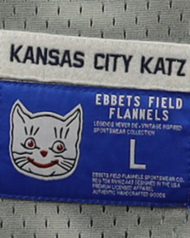 A blue and white label on the EFF Kansas City Katz DNA Replica Button-Up Mesh Jersey features a white cat face with red details, “Kansas City Katz,” “Ban Johnson Baseball League,” EFF, size L, and garment info.