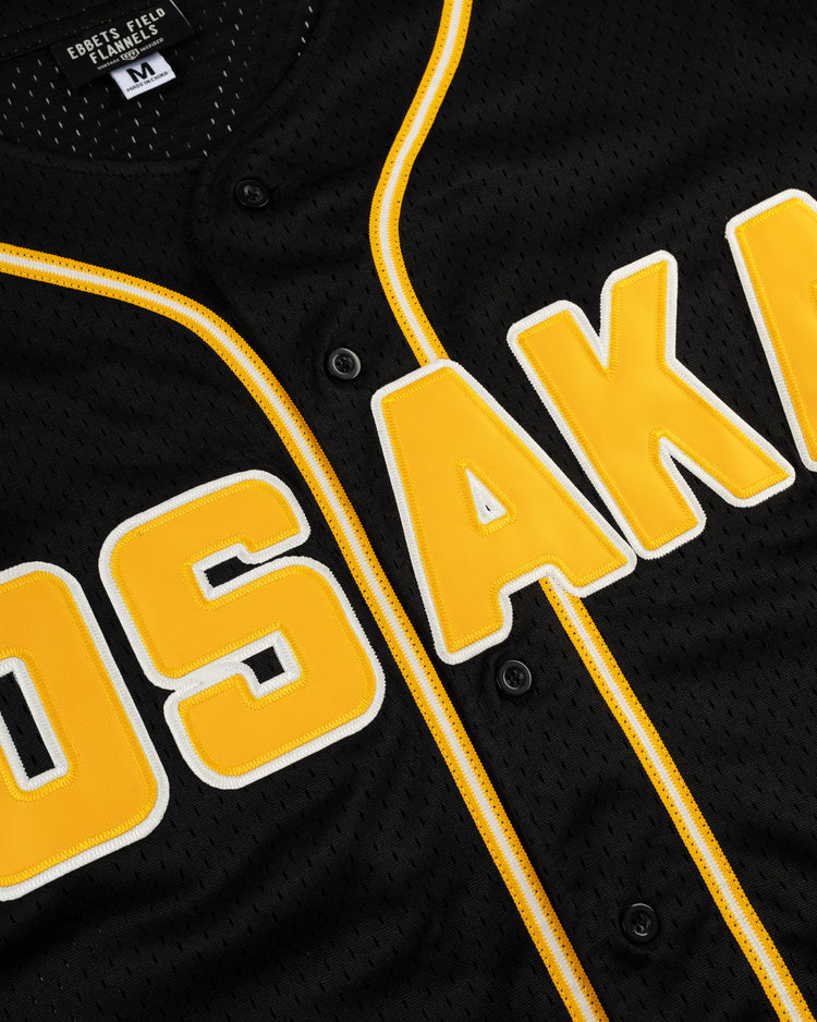 A close-up of the EFF Osaka Tigers Mesh Button-Up Baseball Jersey in black with yellow trim and bold yellow and white OSAKA lettering, inspired by Japans legendary baseball franchise. Features a size M collar tag.