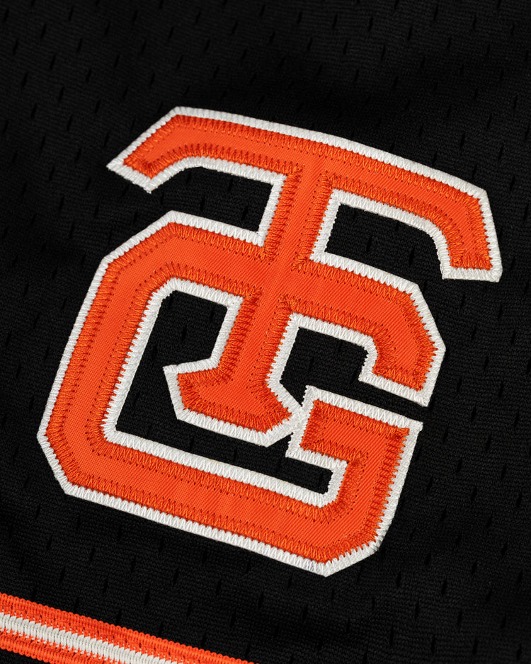 Close-up of an embroidered orange and white G and C logo on the black mesh fabric of the EFF Tokyo Giants Mesh Button-Up Jersey, inspired by classic team sportswear.