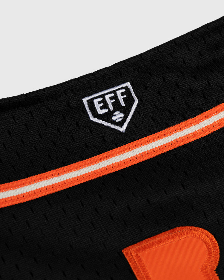Close-up of the Tokyo Giants Mesh Button-Up Jersey by EFF, a vintage-inspired black mesh top with orange and white stripes and a small shield-shaped EFF patch near the neckline, echoing classic Tokyo Giants style.