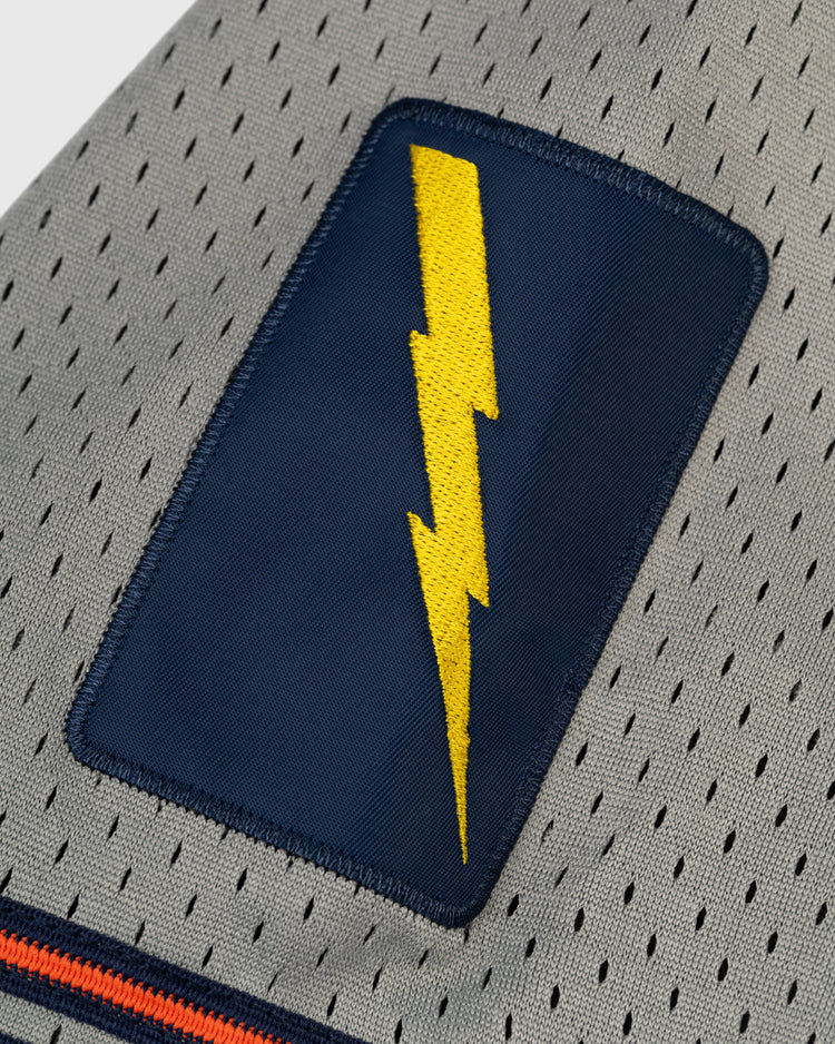 A close-up of the EFF New York Knights Mesh Button-Up Baseball Jersey shows its gray perforated fabric, navy patch with a yellow lightning bolt, and orange and navy stripes inspired by The Natural uniform.