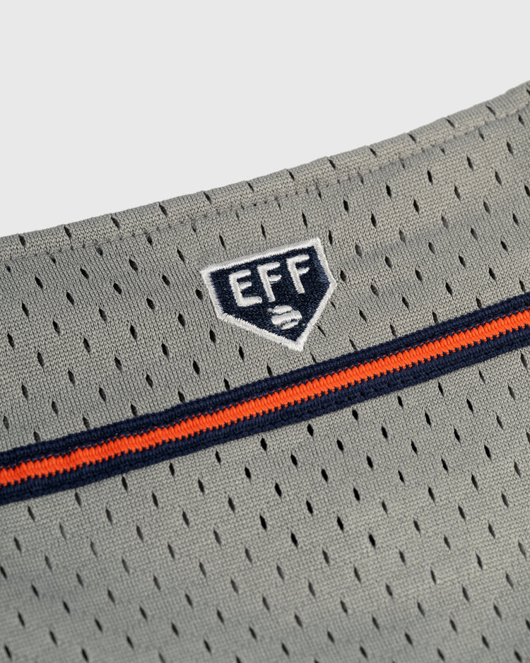 Close-up of the EFF New York Knights Mesh Button-Up Baseball Jerseys gray mesh fabric with perforations, showcasing an embroidered EFF shield logo above navy blue and orange stripes—evocative of vintage jerseys like The Natural.
