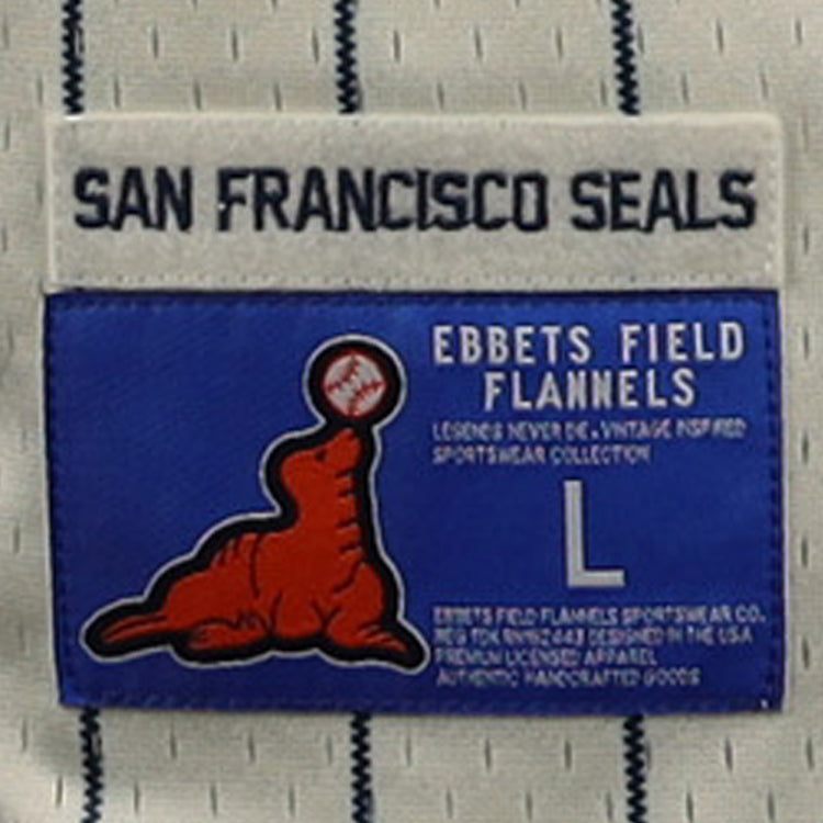 A close-up of the EFF San Francisco Seals DNA Replica Button-Up Mesh Jersey label shows a red seal balancing a baseball, with Ebbets Field Flannels branding and size L, set against a blue background.