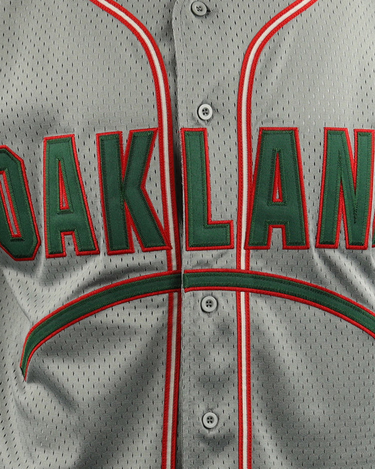 A close-up of the EFF Oakland Oaks EFF DNA Replica Button-Up Mesh Jersey shows bold green and red OAKLAND lettering, with matching trim on the buttons and collar, echoing vintage Pacific Coast League styles.