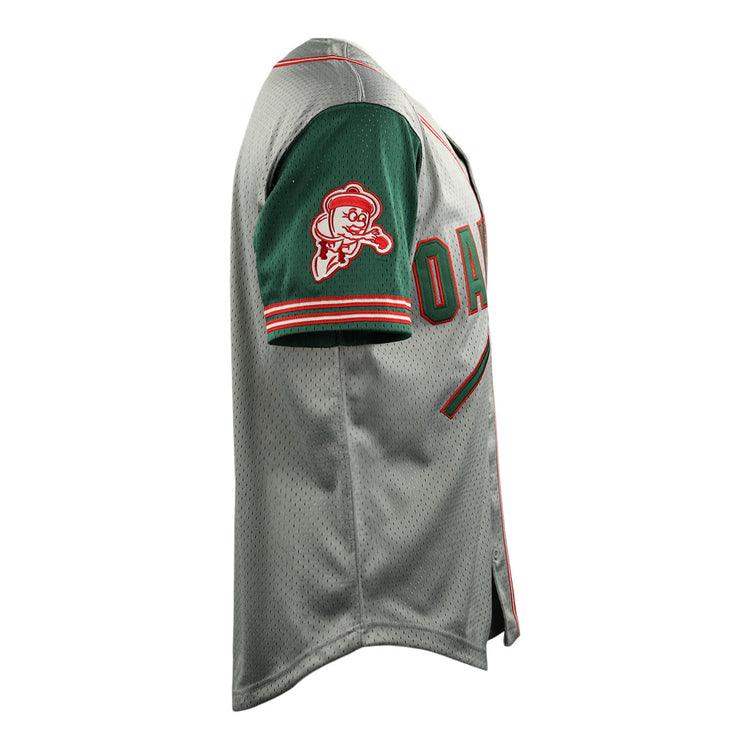 Side view of the Oakland Oaks EFF DNA Replica Button-Up Mesh Jersey by EFF, in gray with a green sleeve, red and white stripes, and a cartoon baseball mascot patch on the sleeve. The chest shows the partial word “OAK,” echoing Pacific Coast League style.