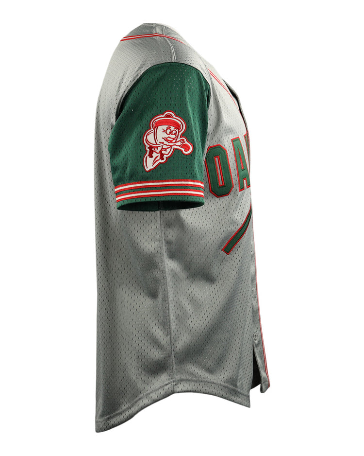 Side view of the Oakland Oaks EFF DNA Replica Button-Up Mesh Jersey by EFF, in gray with a green sleeve, red and white stripes, and a cartoon baseball mascot patch on the sleeve. The chest shows the partial word “OAK,” echoing Pacific Coast League style.