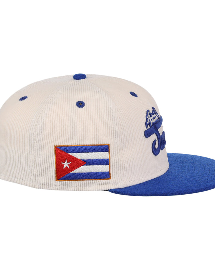 The Santurce Cangrejeros NLB Ground Rule Double Fitted Ballcap by EFF is a white vintage-inspired corduroy hat with a blue brim, embroidered Cuban flag patch on the side, and blue text on the front.