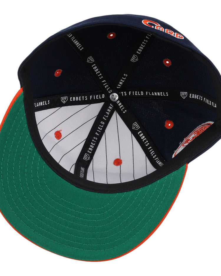 The Hiroshima Carp EFF DNA Fitted Ballcap by EFF is a navy blue vintage cap with a green underbrim, orange stitching on the brim, inner pinstripes, and “EBBETS FIELD FLANNELS” text on black inner bands.