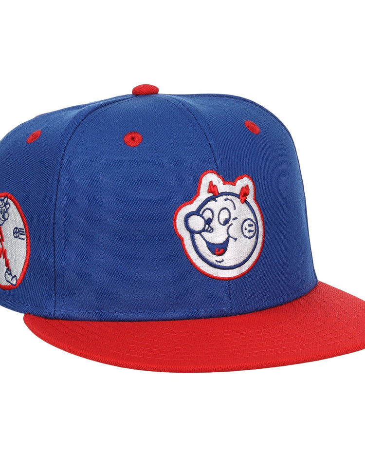The EFF Reddy Kilowatt EFF DNA Fitted Ballcap features a blue vintage design with a red brim, cartoon bear face front, and side patch of a bear playing baseball—classic style inspired by Ebbets Field Flannels.