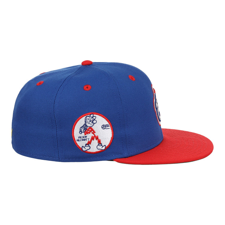 The EFF Reddy Kilowatt EFF DNA Fitted Ballcap features a blue crown, red brim, and an embroidered cartoon bear holding a bat in a red oval patch on the side, inspired by classic Ebbets Field Flannels style.
