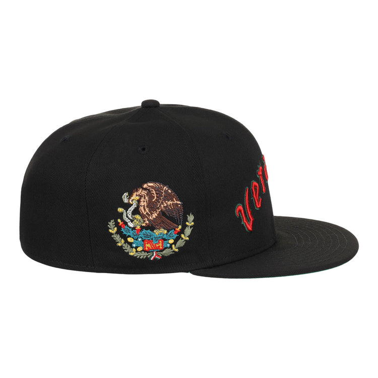 The EFF Veracruz Azules NLB Team Color Fitted Ballcap is a black hat with red cursive text on the front panel and an embroidered Mexican coat of arms on the side.