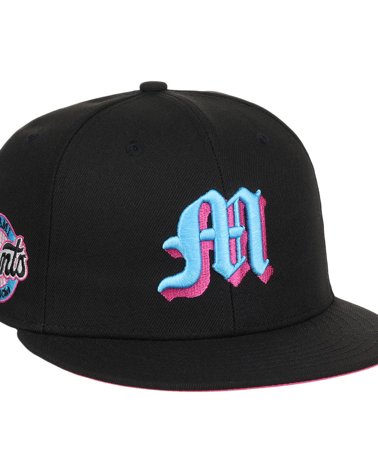 The EFF Miami Giants NLB Team Color Fitted Ballcap is a vintage-inspired black cap with a bold blue and pink M on the front and a matching embroidered San Francisco Giants team logo patch on the side.