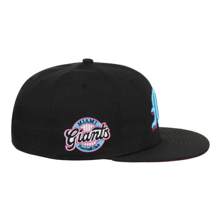 The EFF Miami Giants NLB Team Color Fitted Ballcap is a vintage-inspired black cap with an embroidered light blue M on the front and a pink, blue, and white circular Miami Giants logo on the side, honoring a classic Black barnstorming team.