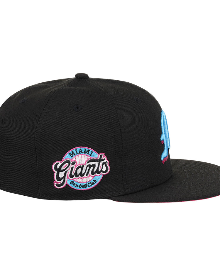 The EFF Miami Giants NLB Team Color Fitted Ballcap is a vintage-inspired black cap with an embroidered light blue M on the front and a pink, blue, and white circular Miami Giants logo on the side, honoring a classic Black barnstorming team.