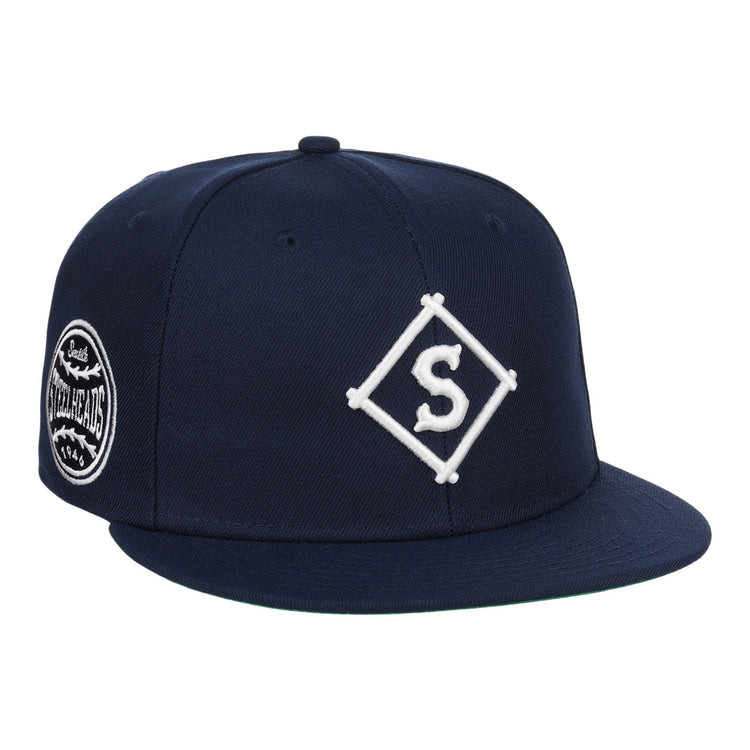The EFF Seattle Steelheads NLB Team Color Fitted Ballcap is a vintage-inspired navy hat with a white diamond S embroidered logo on the front and a circular patch with text and graphics on the side.